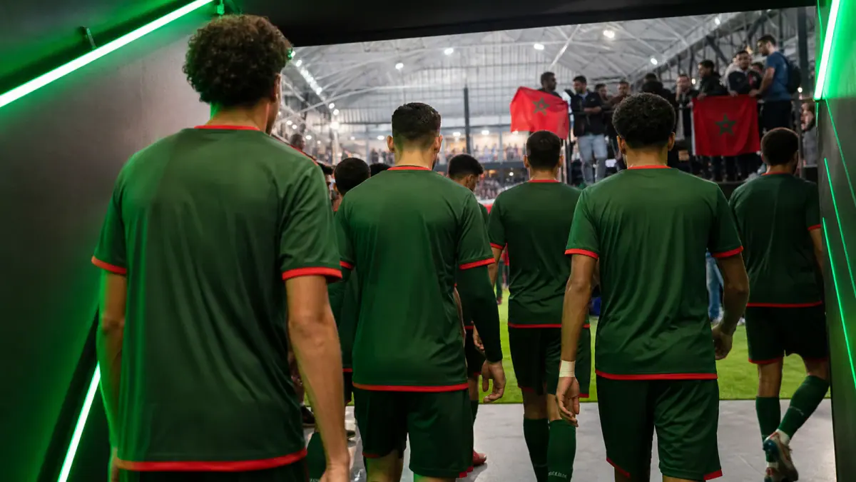 Green-kit football team entering an indoor arena as Moroccan supporters watch