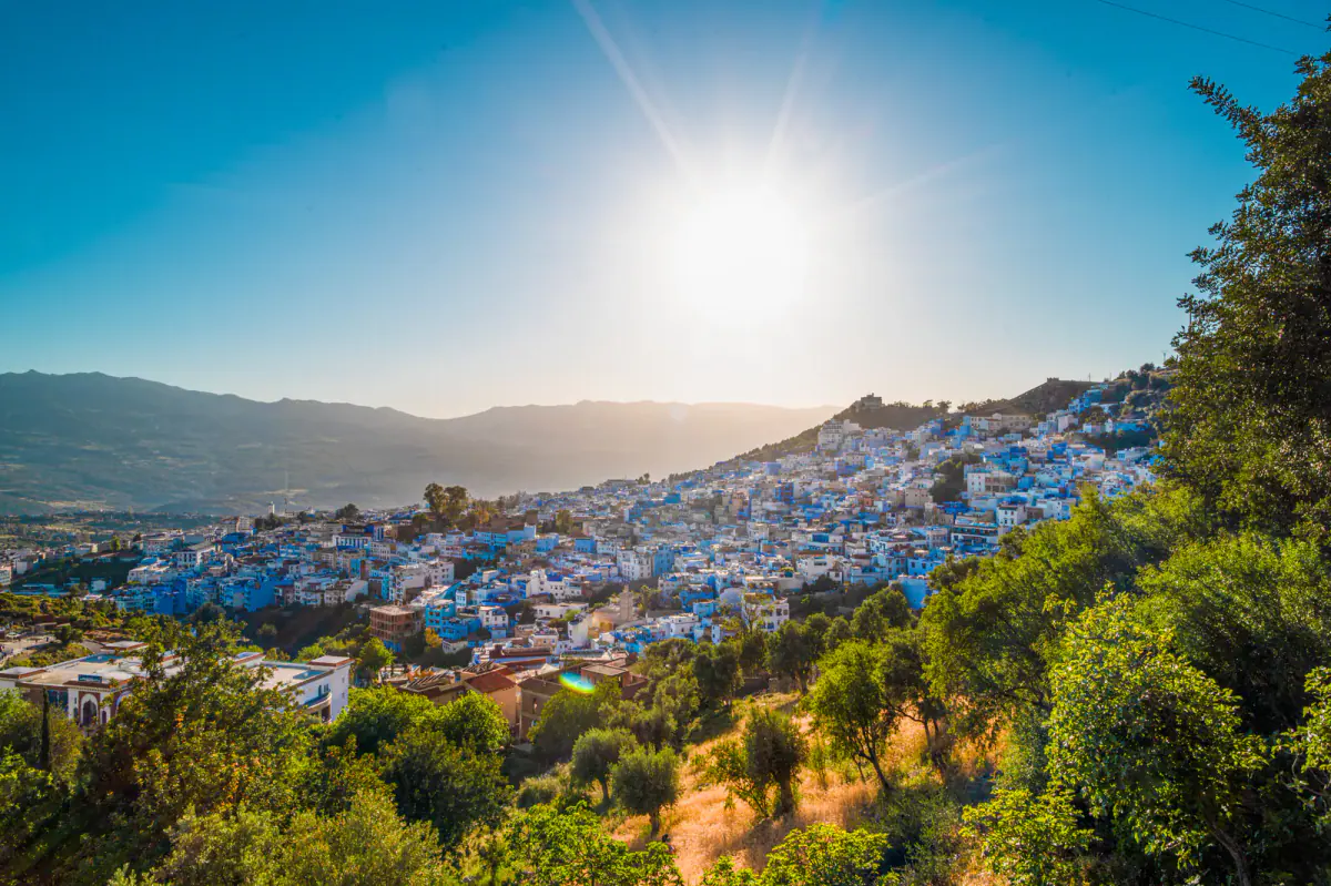 Real sunset photograph of Chefchaouen's blue neighborhoods spread across a Rif Mountain slope